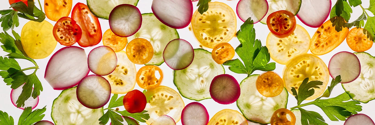 Lay of sliced and halved vegetables on a white background.