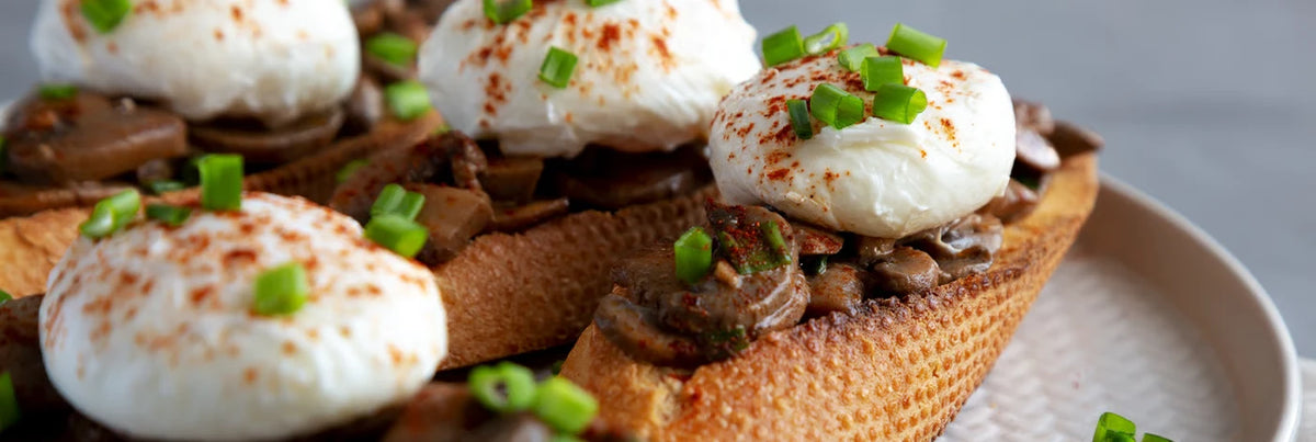 Slices of toasted bread topped with creamy white cheese, brown mushrooms, and chopped green scallions.