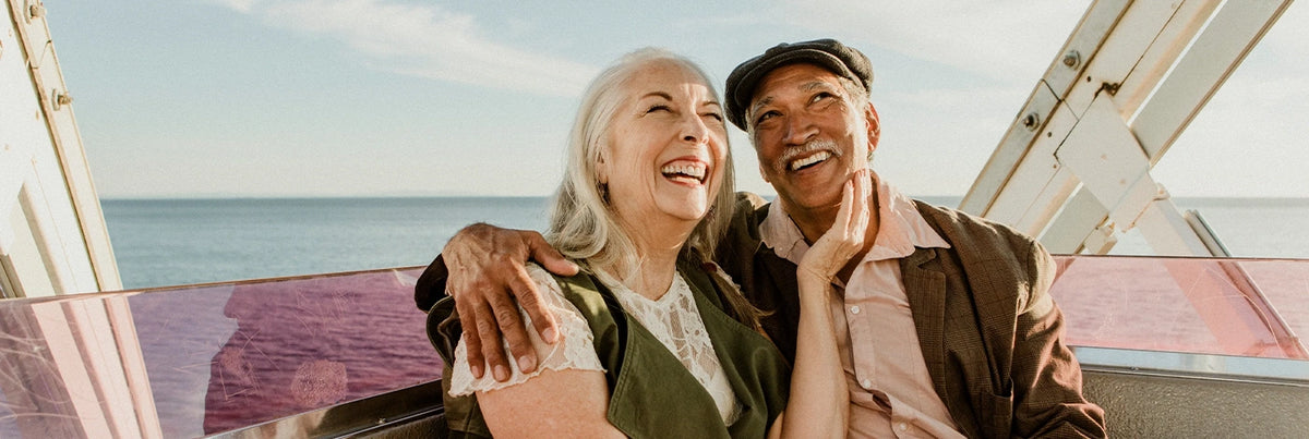 A smiling senior couple posing together on a boat with the ocean and sky in the background.