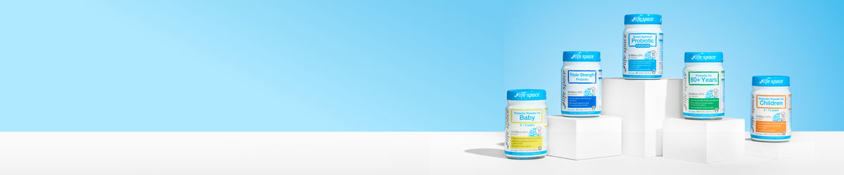 Five supplement bottles with blue caps arranged on white display blocks against a light blue and white studio background.