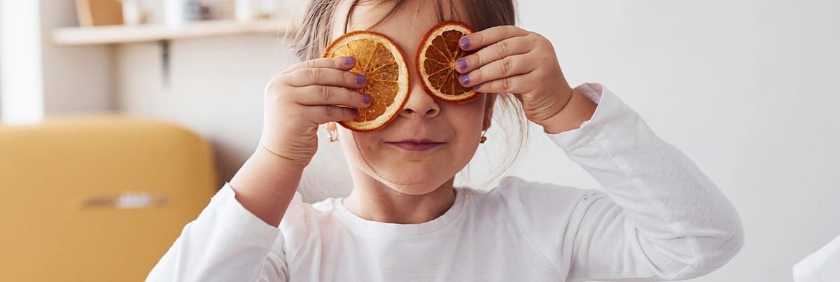 A young girl holds two dried orange slices over her eyes in a playful pose.